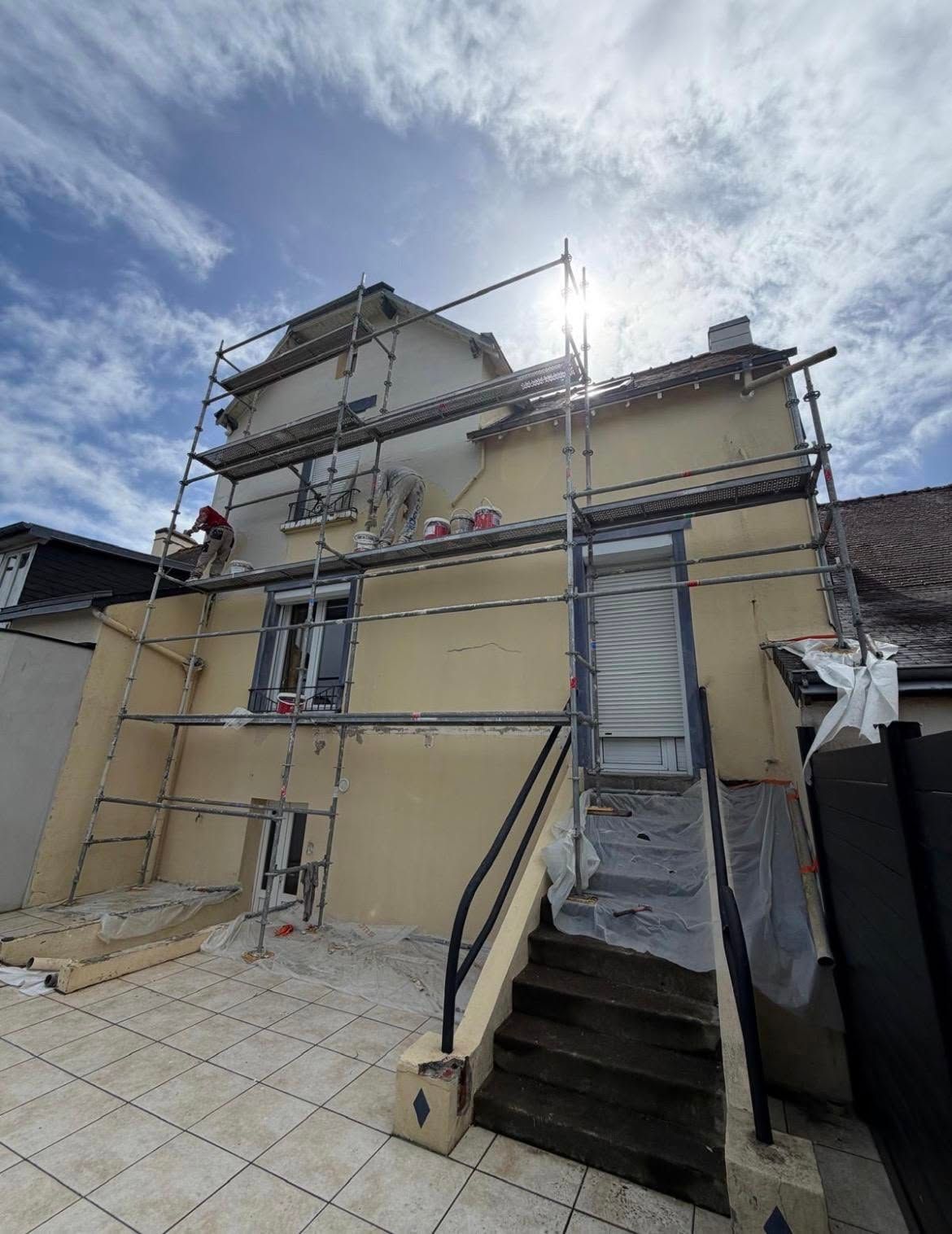 Maison en rénovation avec échafaudages, murs apparents et escalier menant à une entrée principale