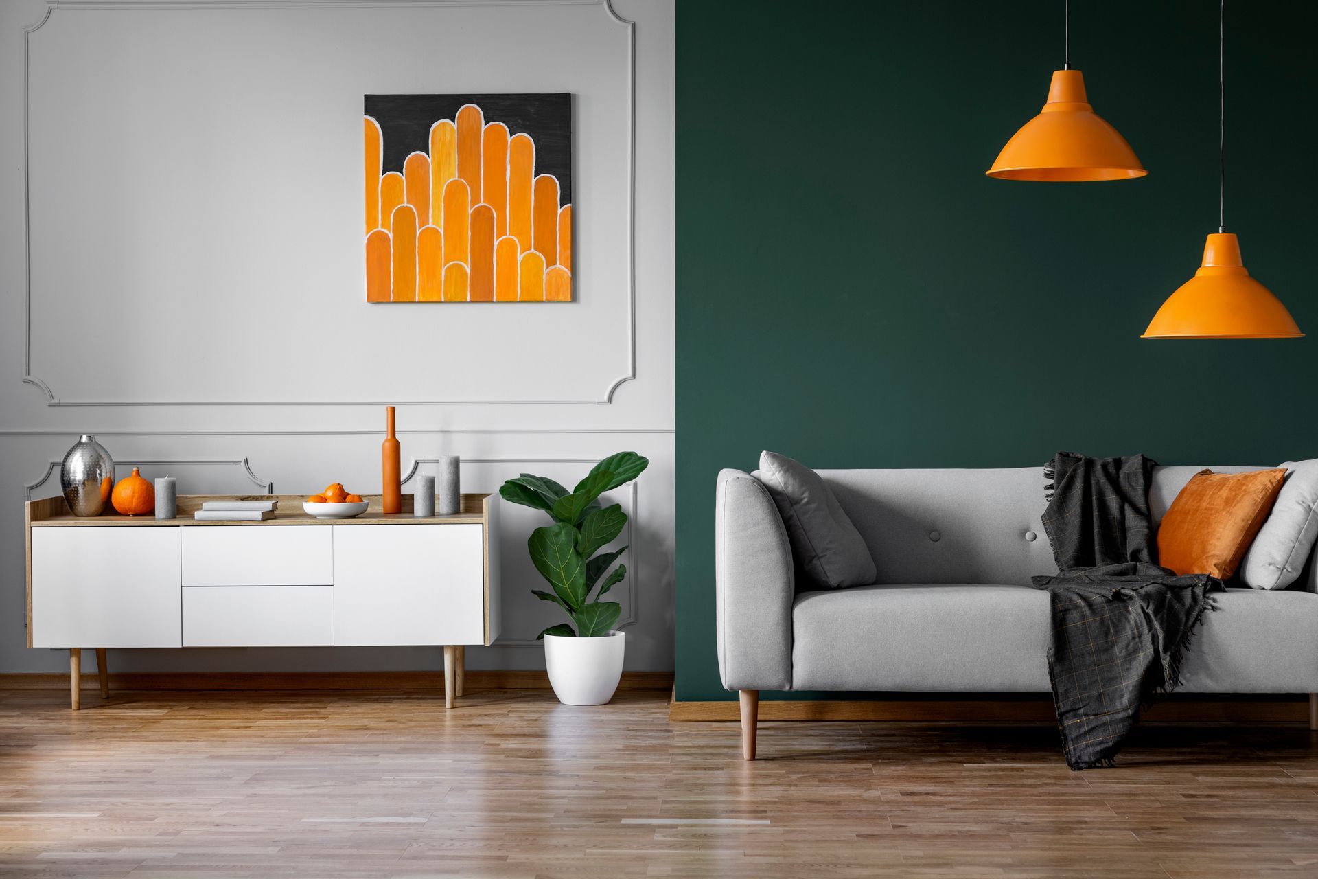 Un salon moderne avec canapés gris, lampes orange et tableaux sur un parquet ciré
