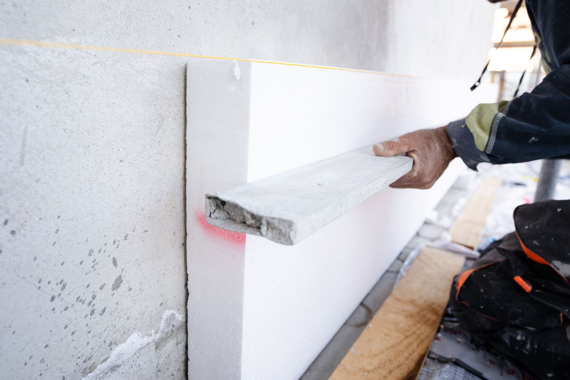 Ouvrier appliquant un panneau isolant blanc sur un mur extérieur