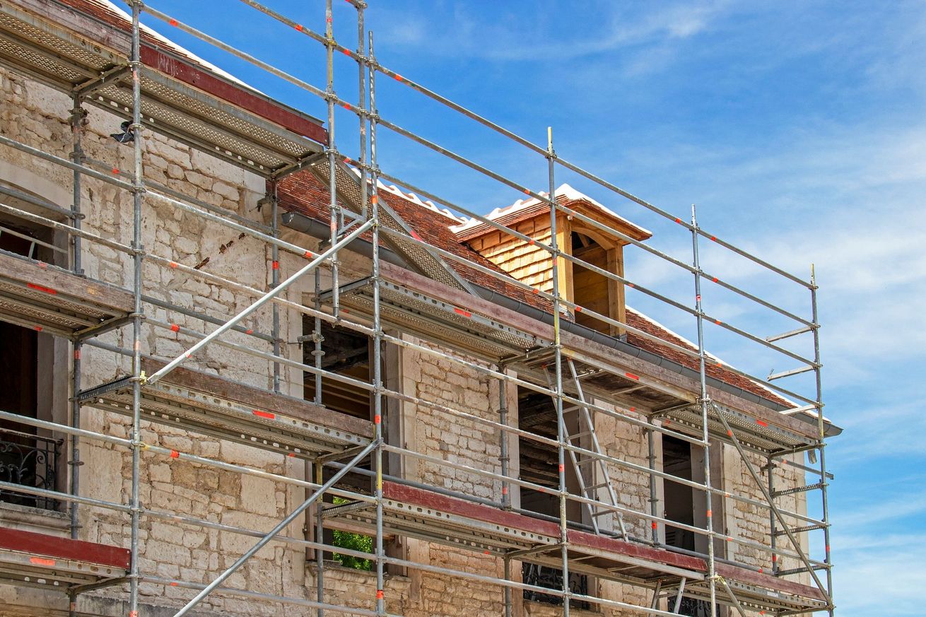 Échafaudages autour d'un bâtiment en briques en construction, sur fond de ciel bleu.