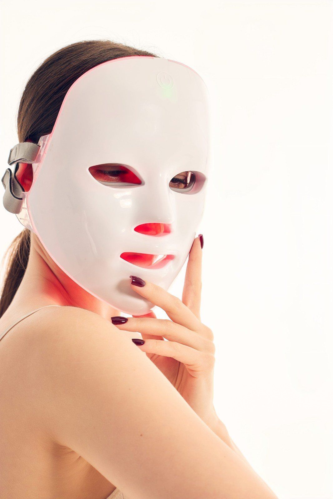 Persona con mascarilla blanca y auriculares, tocándose la barbilla, sobre un fondo blanco brillante