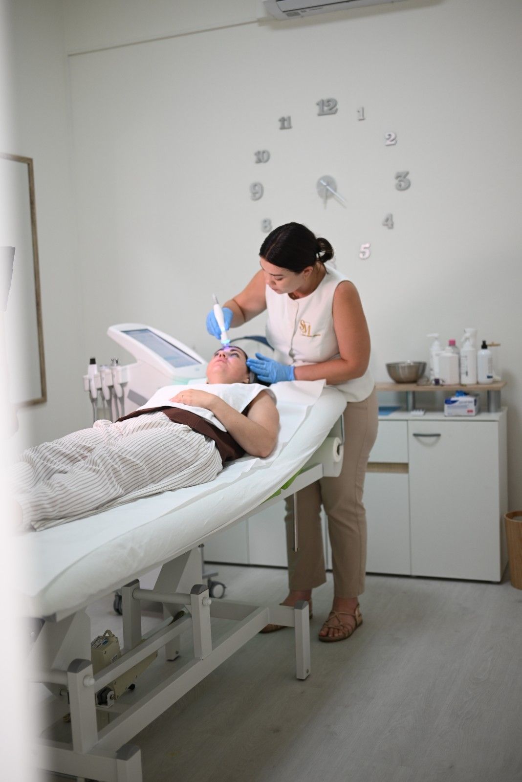 Persona que recibe un tratamiento facial en una sala de spa mientras una esteticista aplica una mascarilla con una brocha