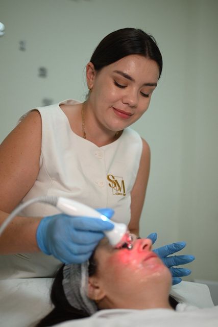 Tratamiento cosmético en curso: un profesional sanitario utiliza un dispositivo luminoso en el rostro de un paciente reclinado