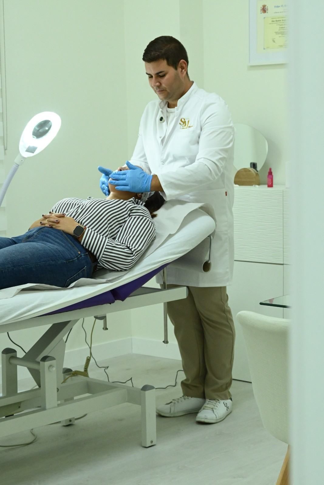 Dentista atendiendo a un paciente en una clínica, con mascarilla azul y una lámpara dental cerca.