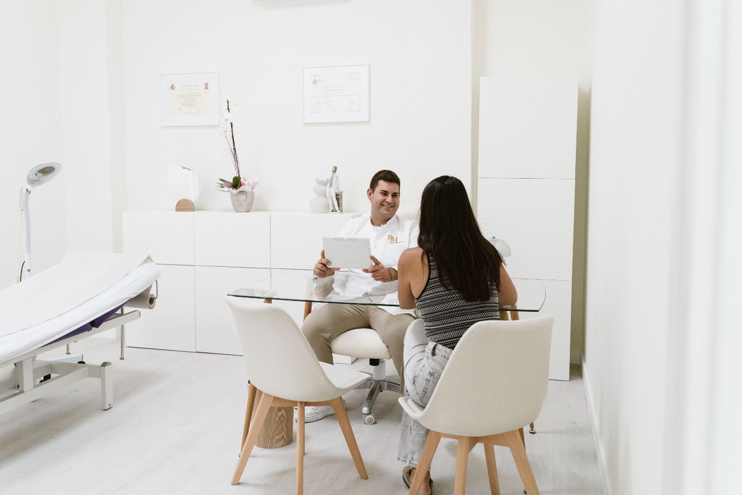 Dos personas conversando en un escritorio blanco y luminoso, en una sala limpia con aspecto de clínica