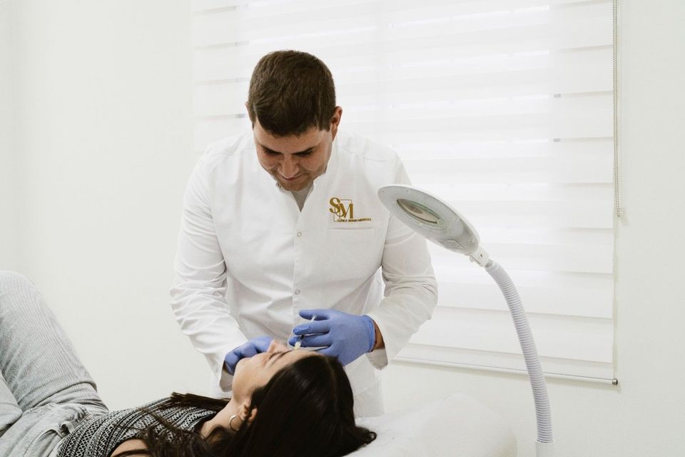 Persona que recibe un tratamiento facial en una sala de spa mientras una esteticista aplica una mascarilla con una brocha