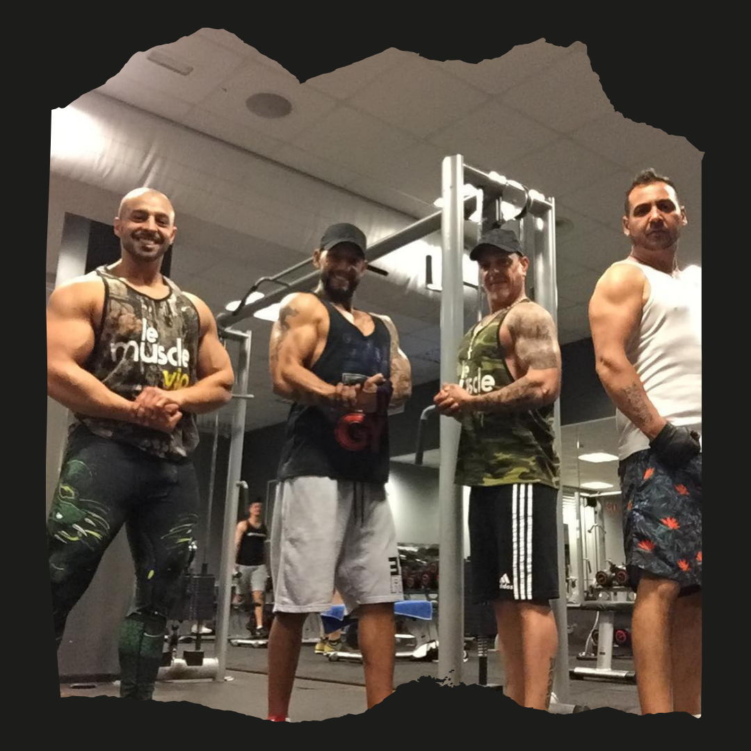 Cuatro hombres posan para una foto en un gimnasio y uno de ellos lleva una camiseta sin mangas que dice