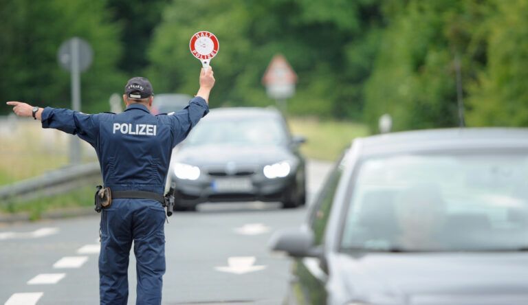 Ein Polizist regelt den Verkehr auf einer Straße, im Hintergrund fahren Autos vorbei.
