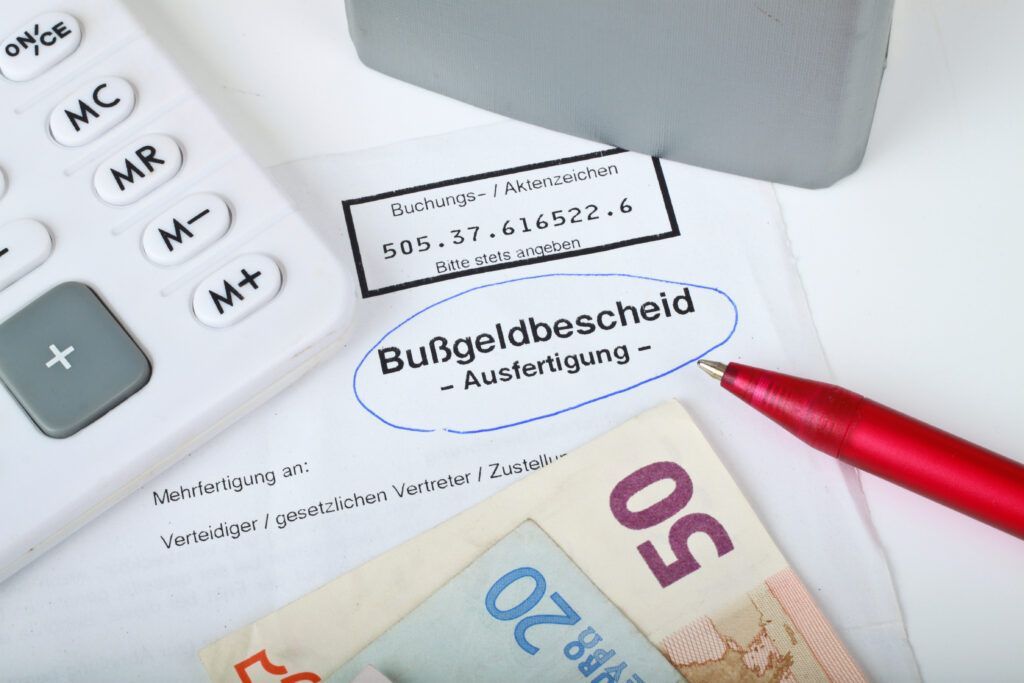 Strafzettel für Falschparken mit Taschenrechner, rotem Stift und Euro-Banknoten auf einem Schreibtisch