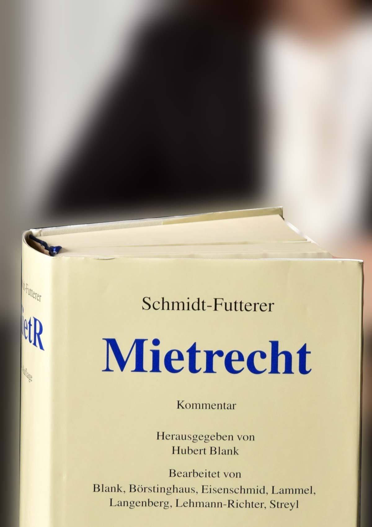 Ein beigefarbenes deutsches Gesetzbuch „Mietrecht“ mit blauem Titel, aufrecht vor einem verschwommenen Hintergrund gehalten.