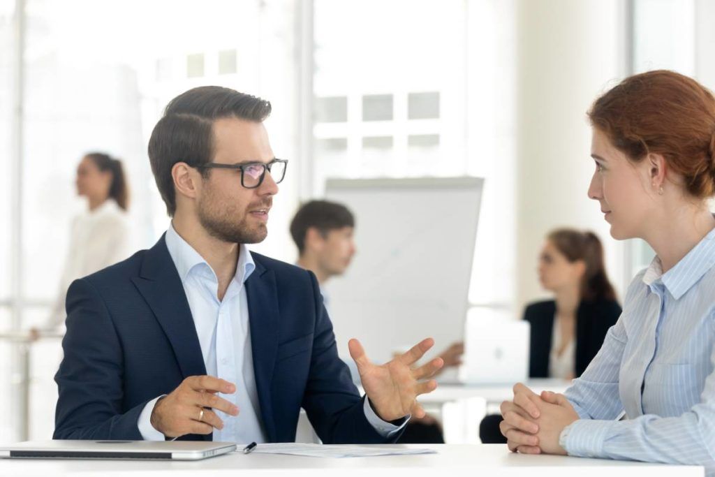 Zwei Arbeitskollegen unterhalten sich an einem Schreibtisch in einem hellen Büro