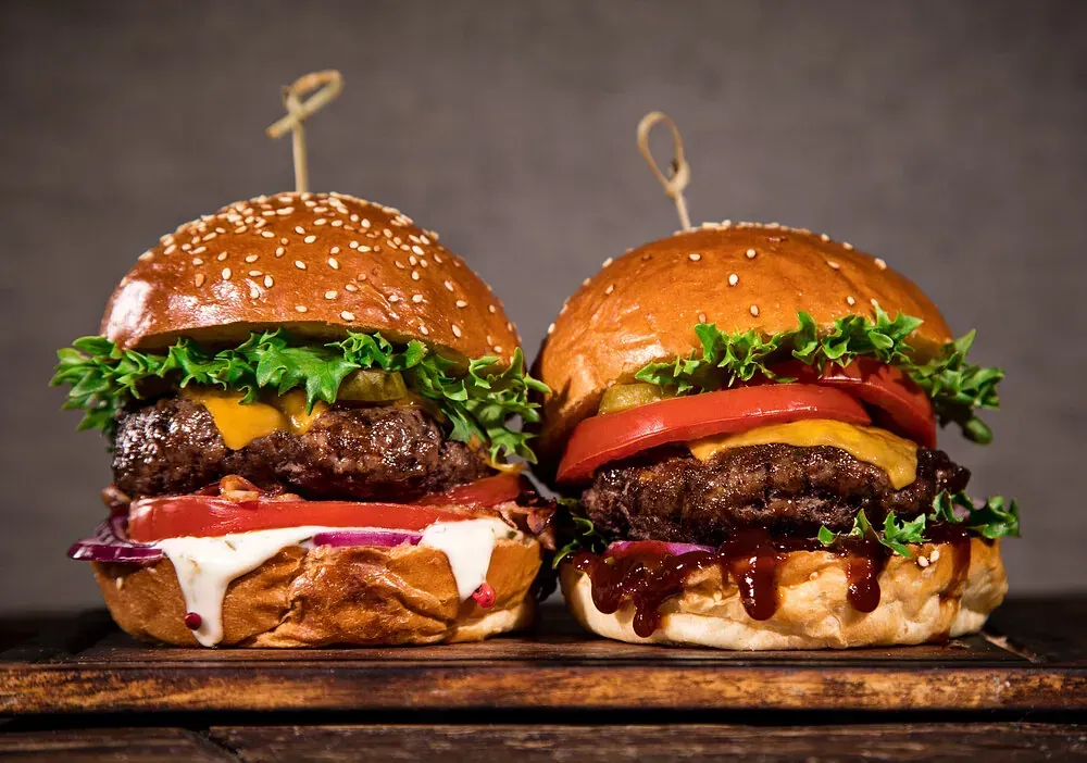 Dos hamburguesas están sentadas sobre una tabla de cortar de madera.