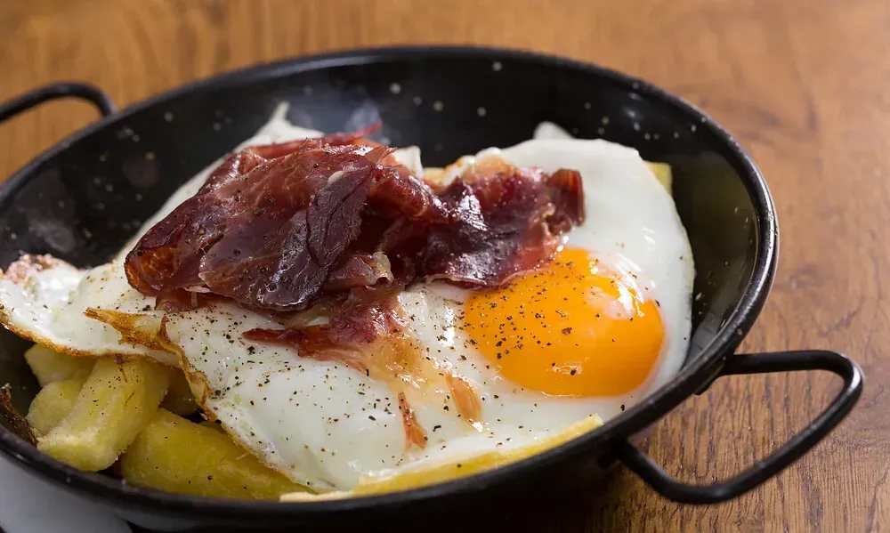 Una sartén llena de huevos y patatas sobre una mesa de madera.