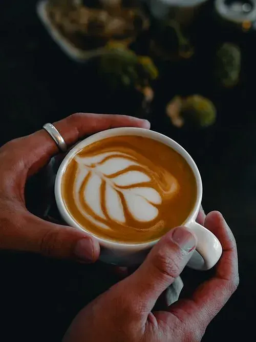 Una persona sostiene una taza de café con arte latte en ella.