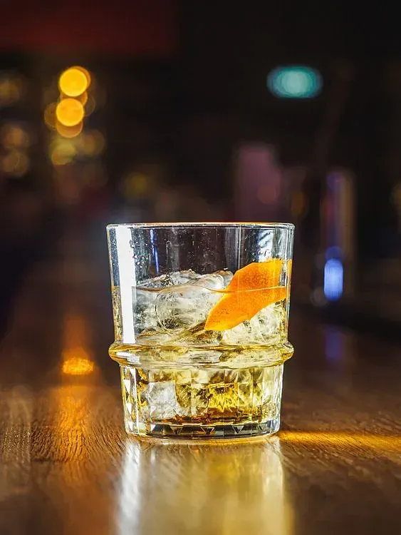 Un vaso de whisky con hielo y una cáscara de naranja sobre una mesa de madera.