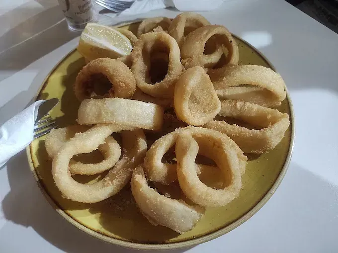 Un plato amarillo cubierto con aros de cebolla fritos y una rodaja de limón.