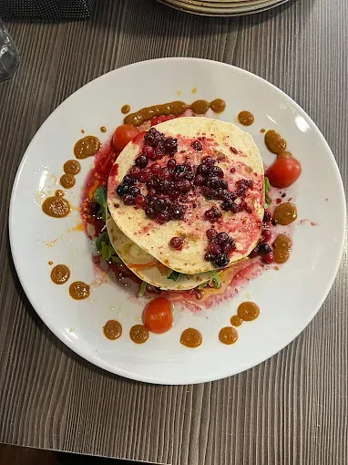 Un plato blanco cubierto con una pila de panqueques y bayas.