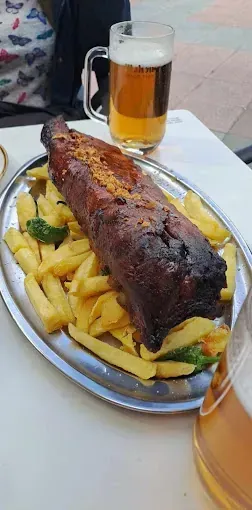 Un plato de comida con costillas y patatas fritas en una mesa junto a un vaso de cerveza.