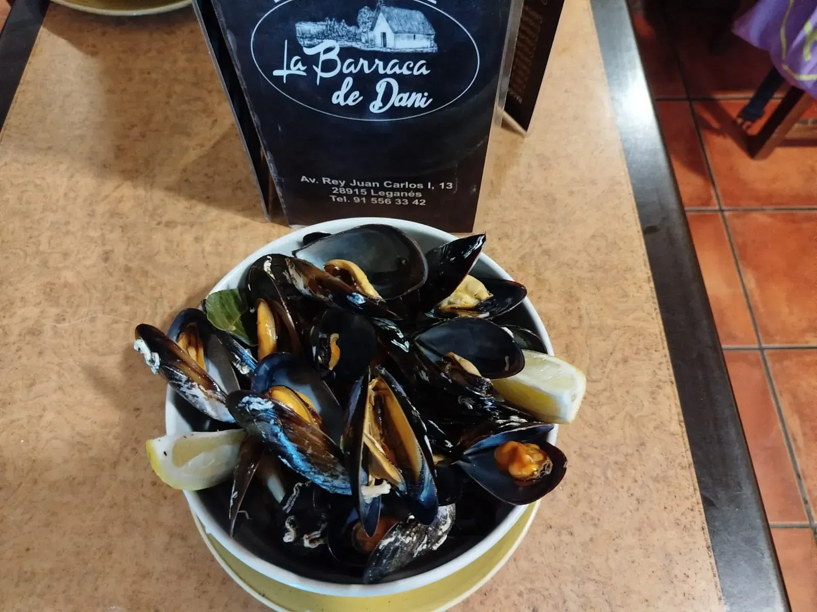 Un tazón de mejillones se encuentra en una mesa junto a un menú de la barraca de dan