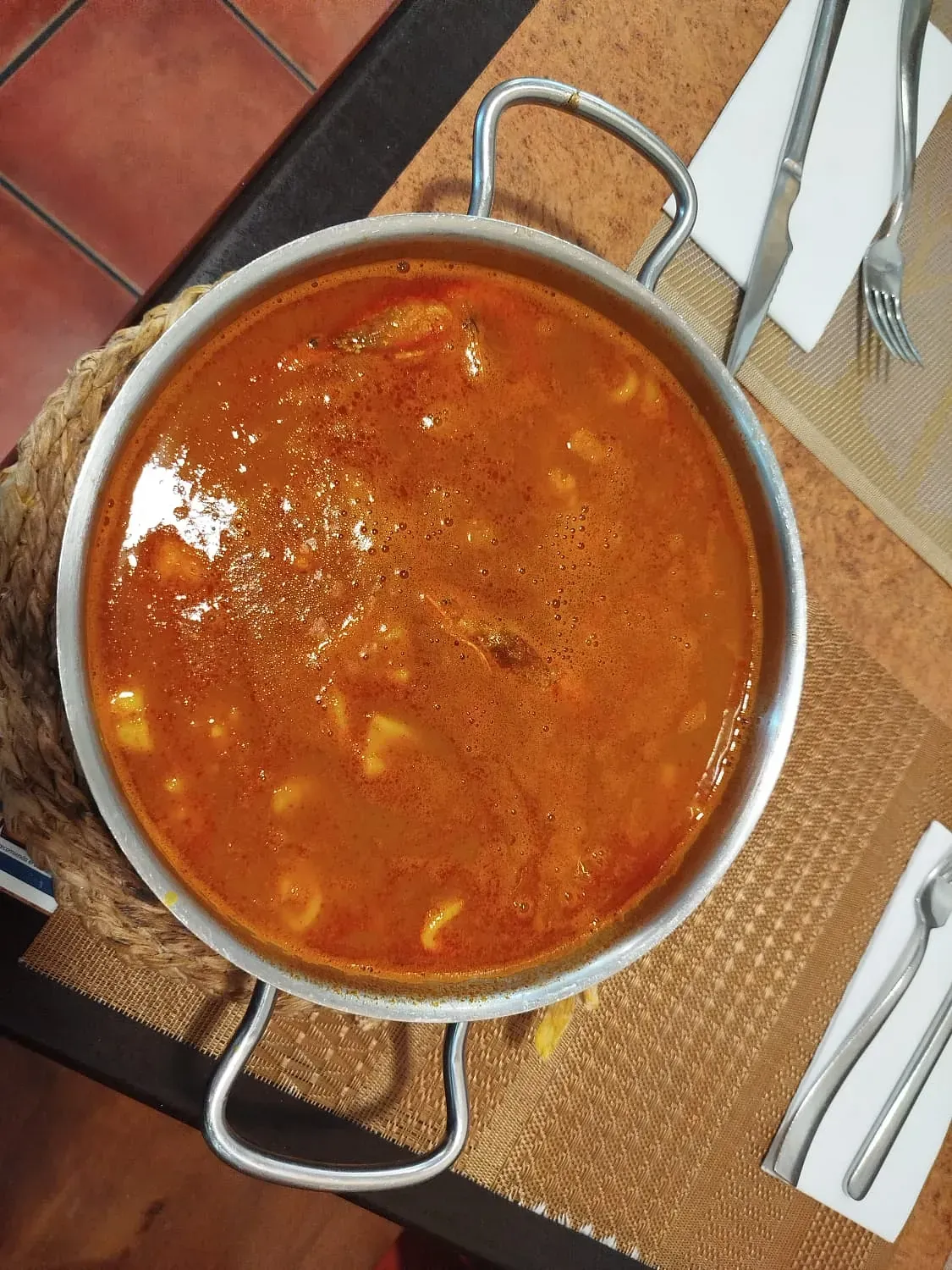 Una olla de sopa reposa sobre una mesa con utensilios.