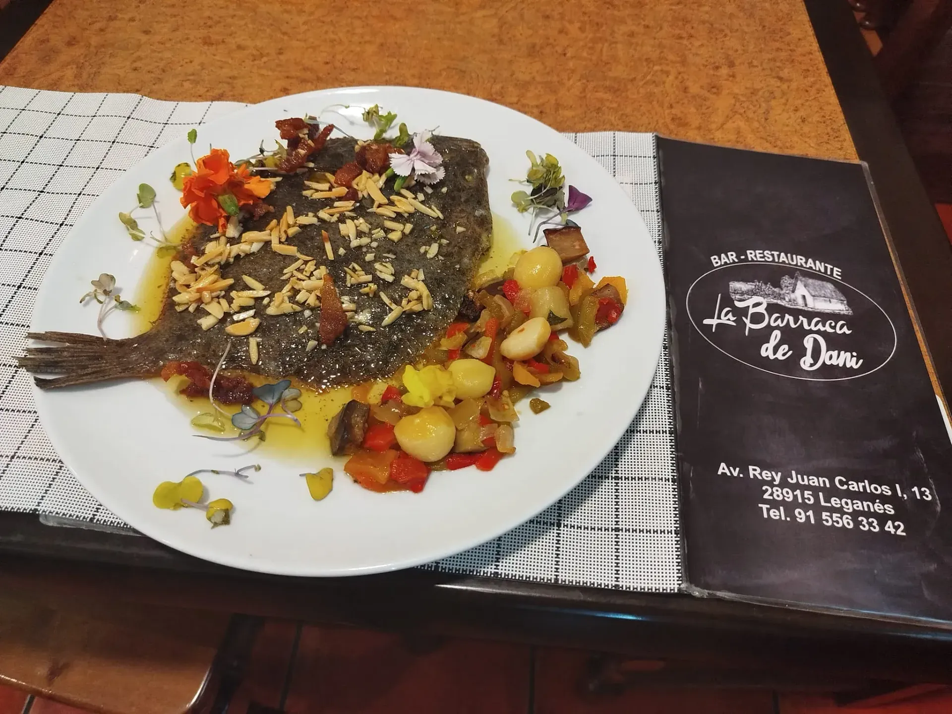 Un plato blanco con pescado y verduras al lado de un menú.