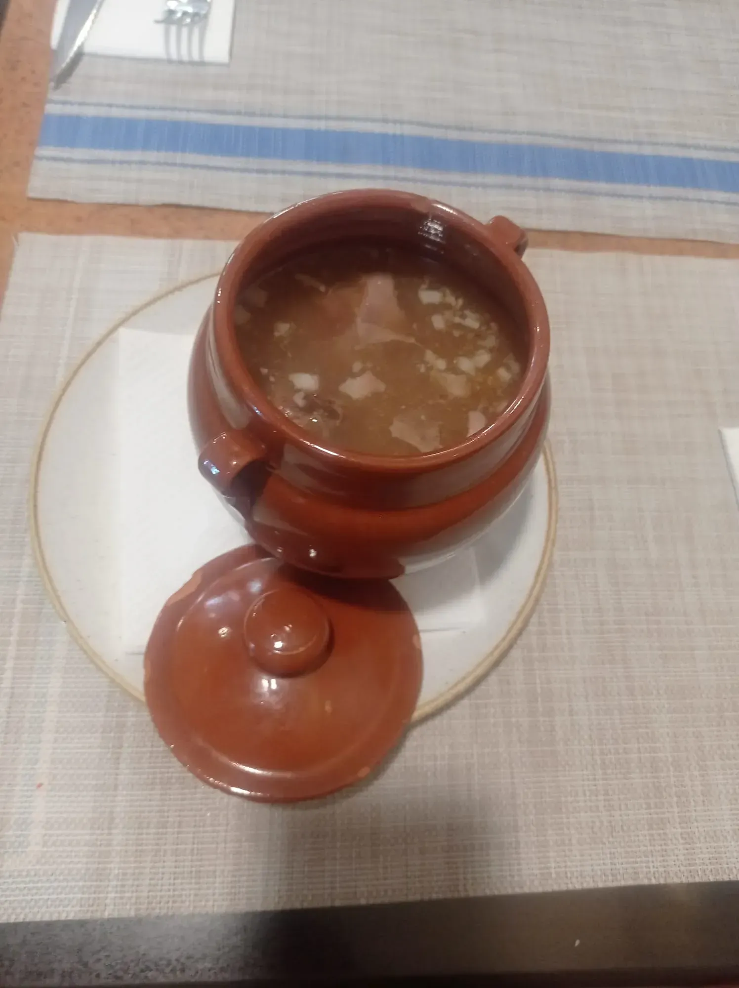 Un tazón de sopa reposa en un plato sobre una mesa.