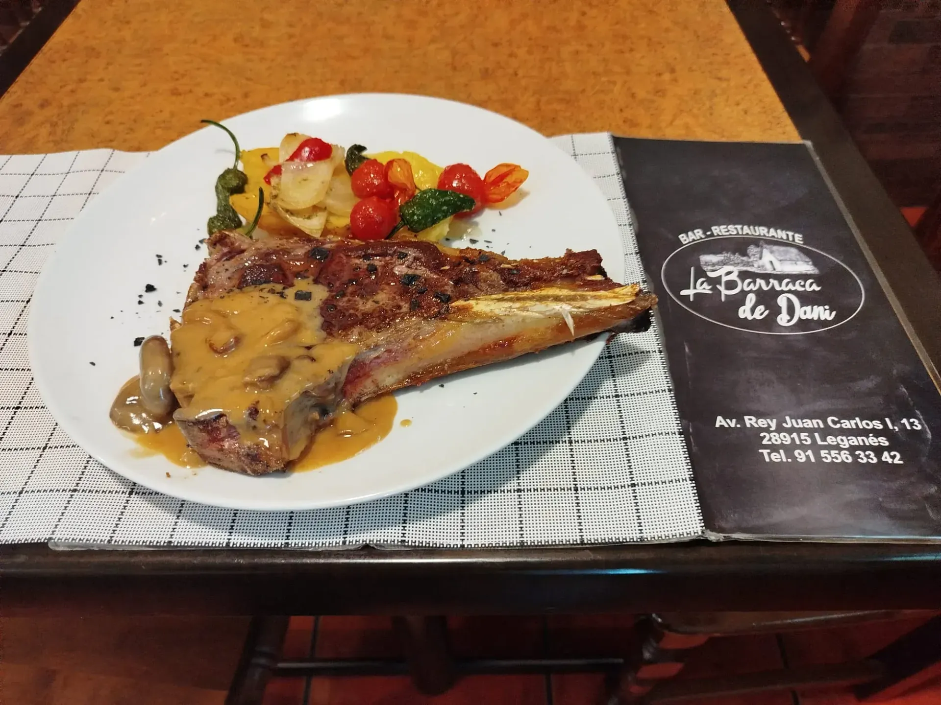 Un plato blanco cubierto con carne y verduras junto a un menú de la barraca de doña.