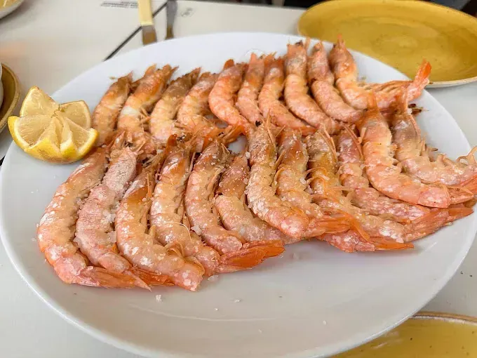 Un plato blanco cubierto con camarones y una rodaja de limón.
