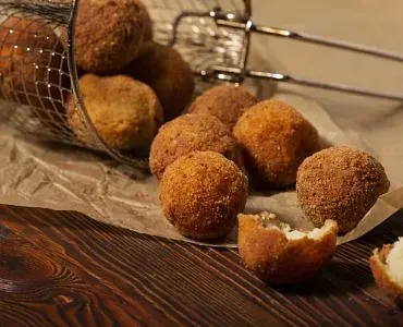 Una cesta llena de bolas de comida frita sobre una mesa de madera.