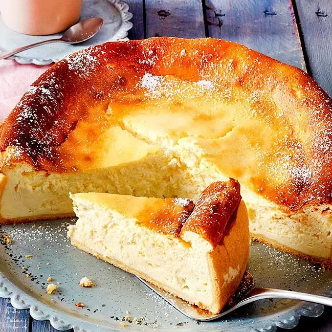 Una tarta de queso de la que se ha sacado un trozo con un tenedor y lo hemos colocado en un plato.