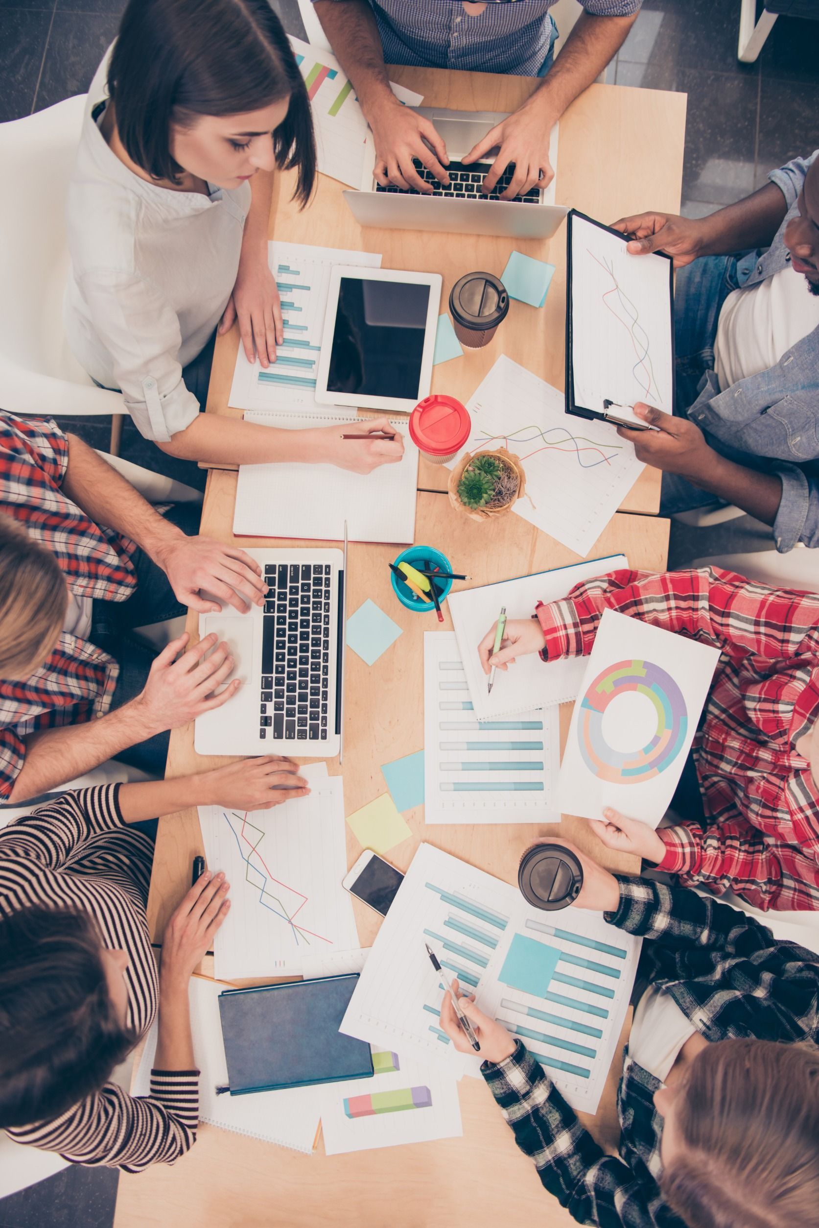 Un grupo de personas están sentadas alrededor de una mesa con computadoras portátiles y papeles.