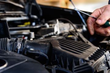 Un mecánico inspecciona el compartimento del motor de un coche con una herramienta cerca de la entrada de aire.