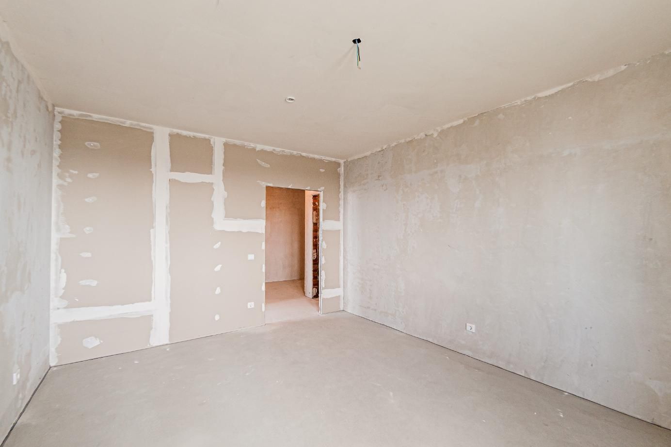 Habitación vacía sin terminar, con paredes de pladur al descubierto, suelo blanco y una puerta abierta.