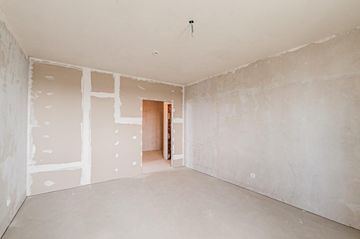 Habitación vacía sin terminar, con paredes de pladur al descubierto, suelo blanco y una puerta abierta.