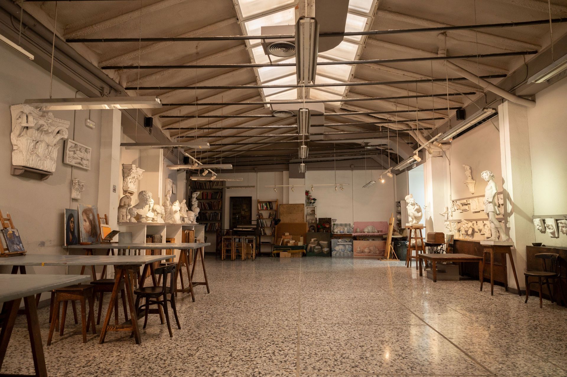 Estudio de arte con esculturas, mesas y techo alto.