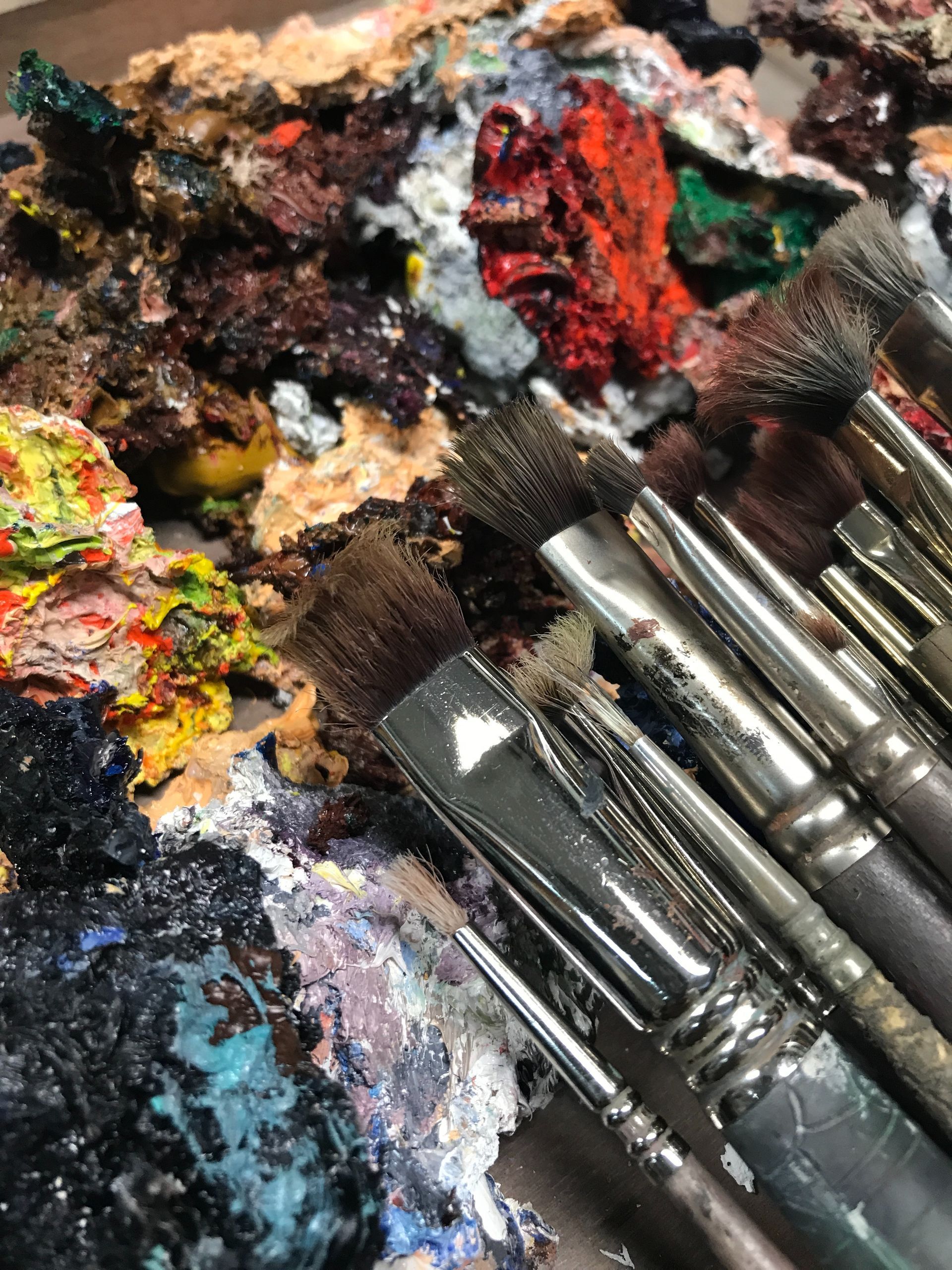 Pinceles sobre una paleta de artista colorida, con pintura seca de varios colores.