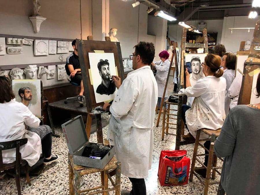 Clase de arte: Estudiantes con batas blancas pintan y observan un retrato. Estudio con moldes y materiales.