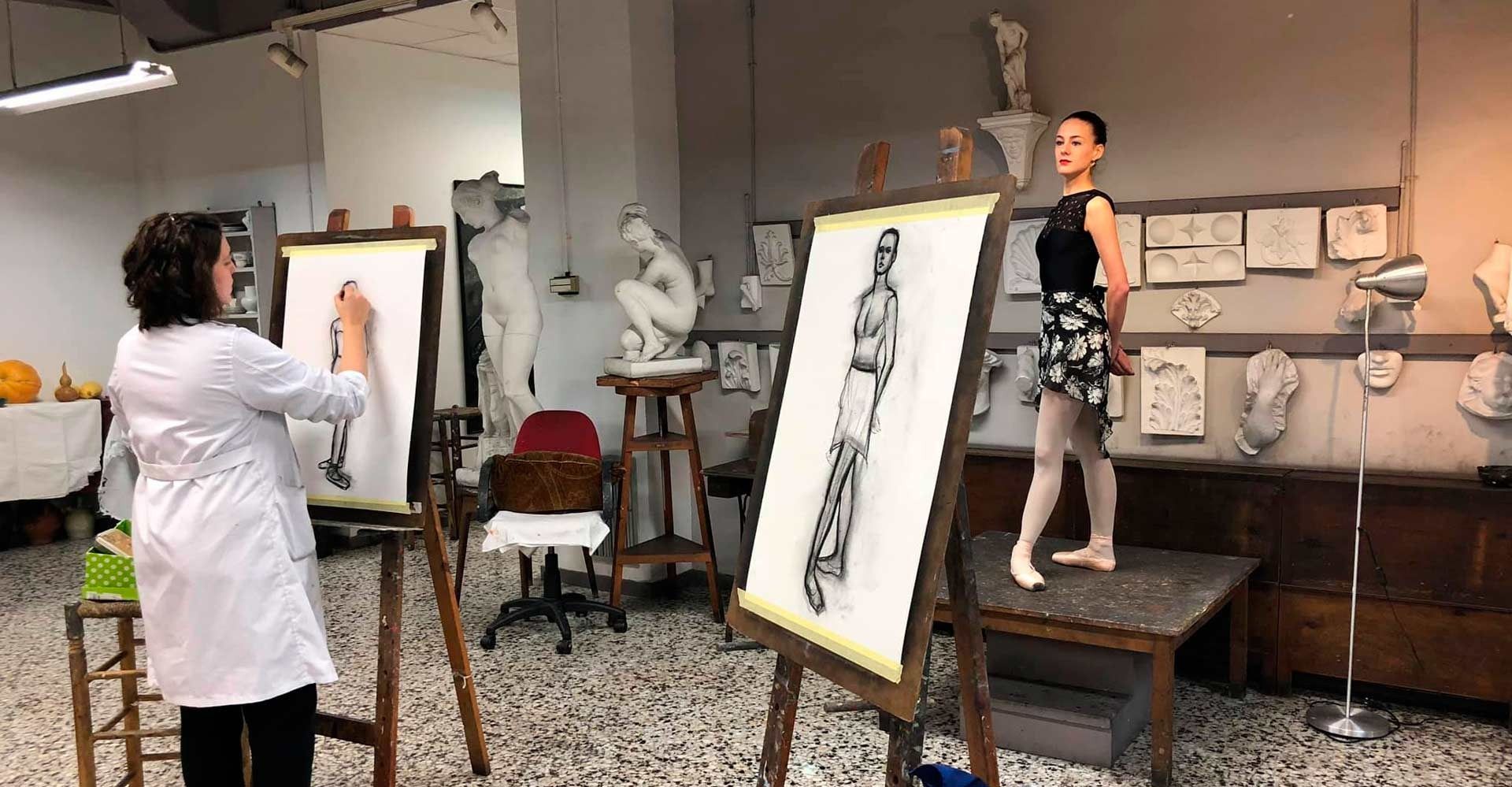 Artista dibujando a una bailarina en un estudio. La bailarina posa, con dibujos en caballetes en primer plano.