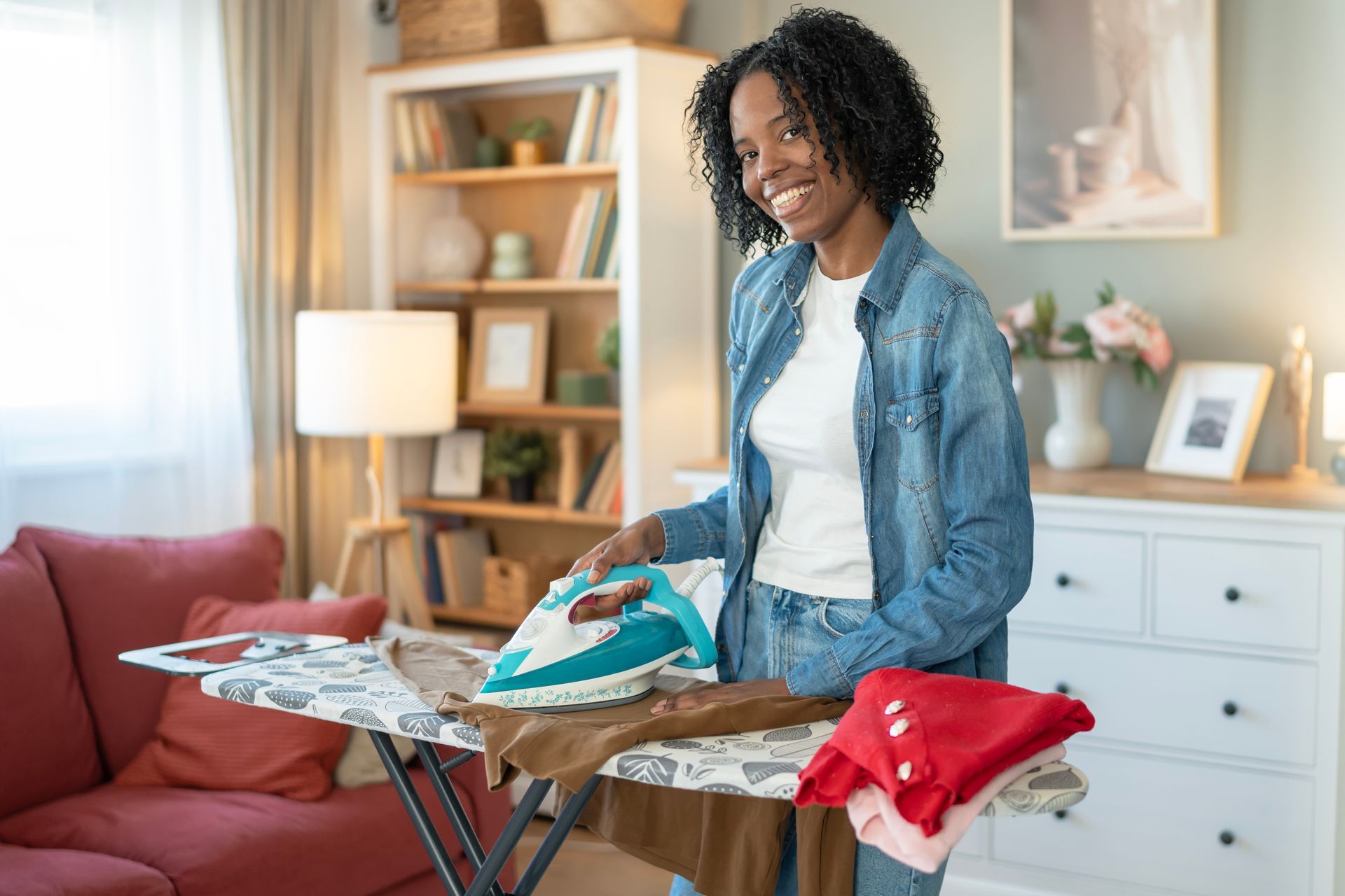 Une personne repasse du linge dans un salon lumineux, avec du linge plié sur une planche à repasser.