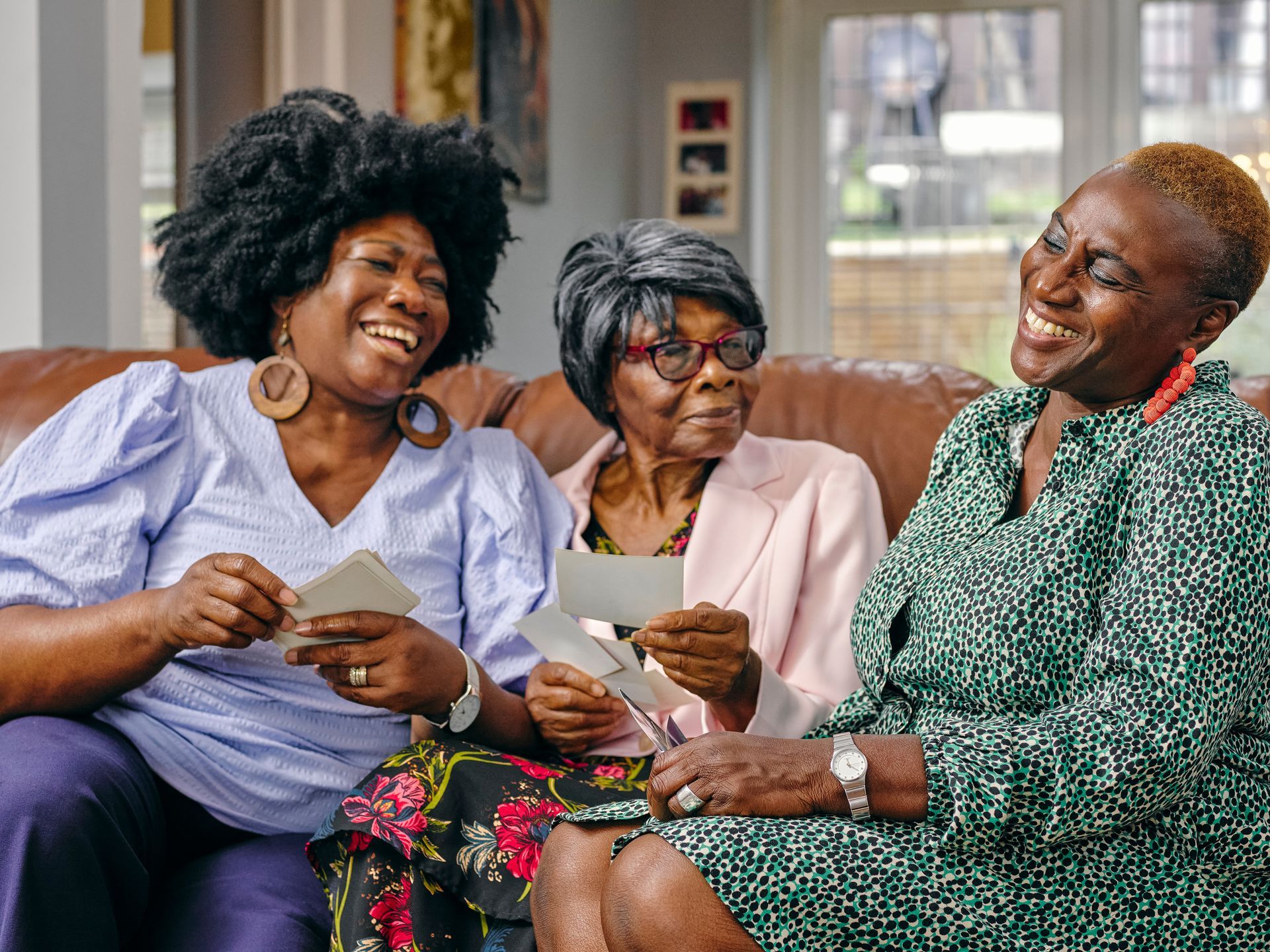 Trois personnes sont assises sur un canapé, souriantes et discutant, un verre à la main.