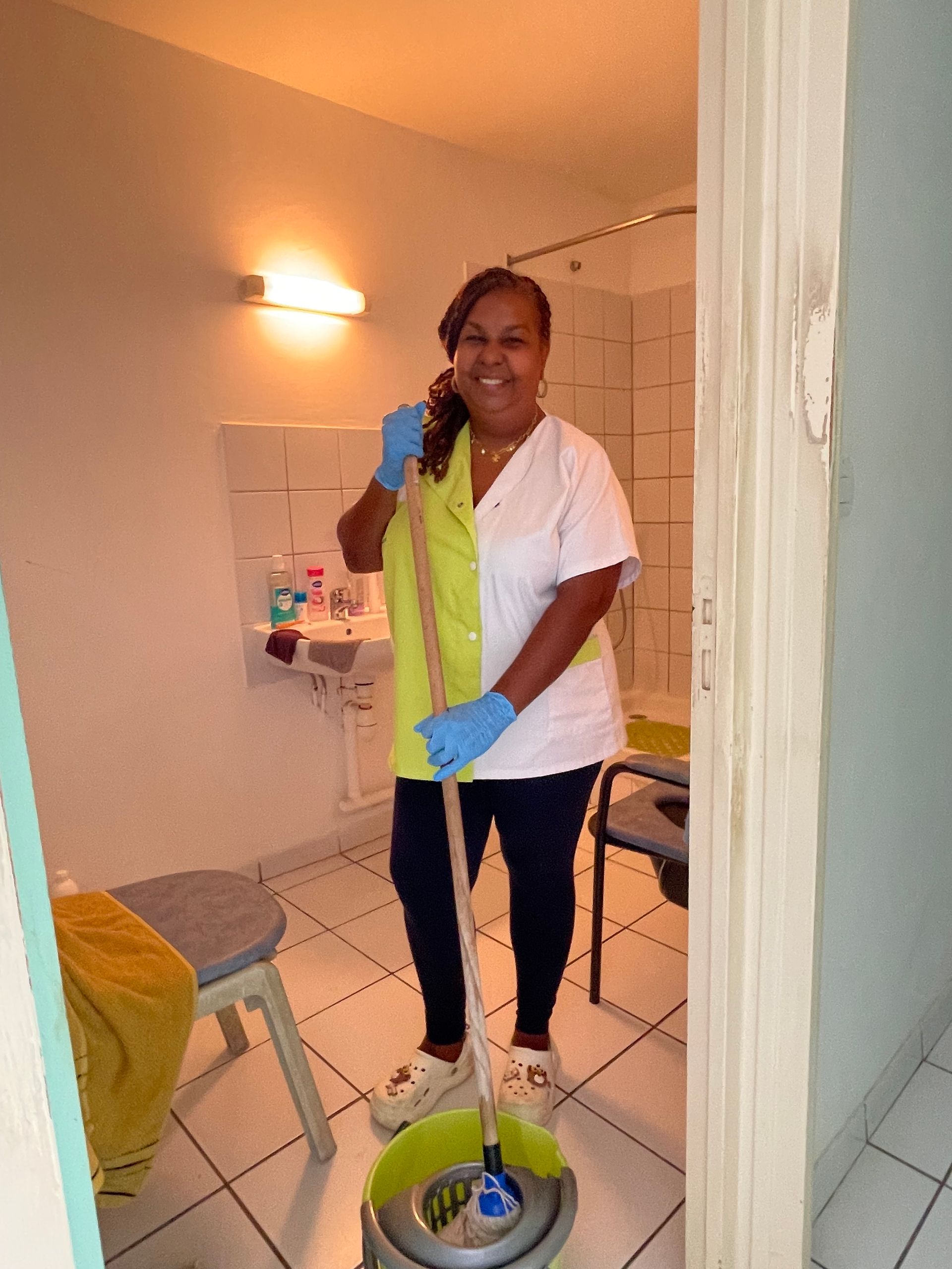 Une femme passe l'aspirateur dans un salon avec un canapé rouge, une commode blanche et des plantes d'intérieur.