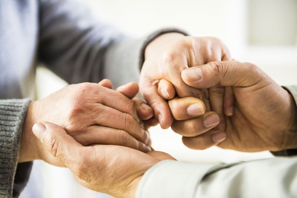 Deux mains tenant délicatement la main jointe d'une personne, en gros plan sous une lumière douce.