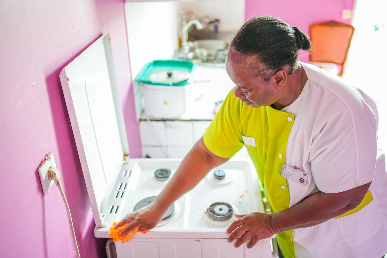 Une personne examine les boutons d'une cuisinière blanche dans une cuisine rose avec un miroir mural.