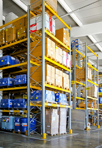 Estanterías industriales amarillas en un almacén, repletas de cajas y barriles azules.