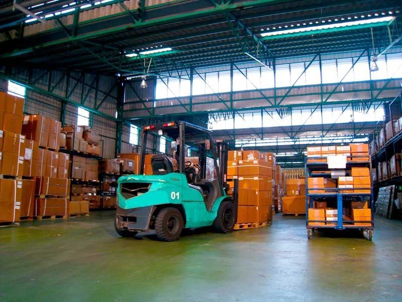 Carretilla elevadora en un almacén, moviendo cajas. Las cajas están apiladas en estanterías y en el suelo. Carretilla elevadora verde.