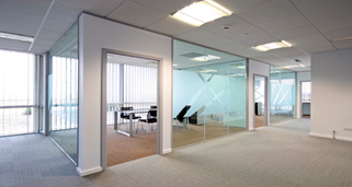 Oficina vacía con habitaciones con paredes de vidrio, alfombra beige y una iluminación superior brillante.