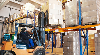 Operador de montacargas en un almacén levantando cajas y colocándolas en un estante.