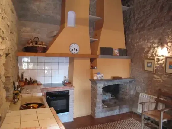 Cocina de piedra con estufa de azulejos, chimenea de leña y paredes de color beige cálido.