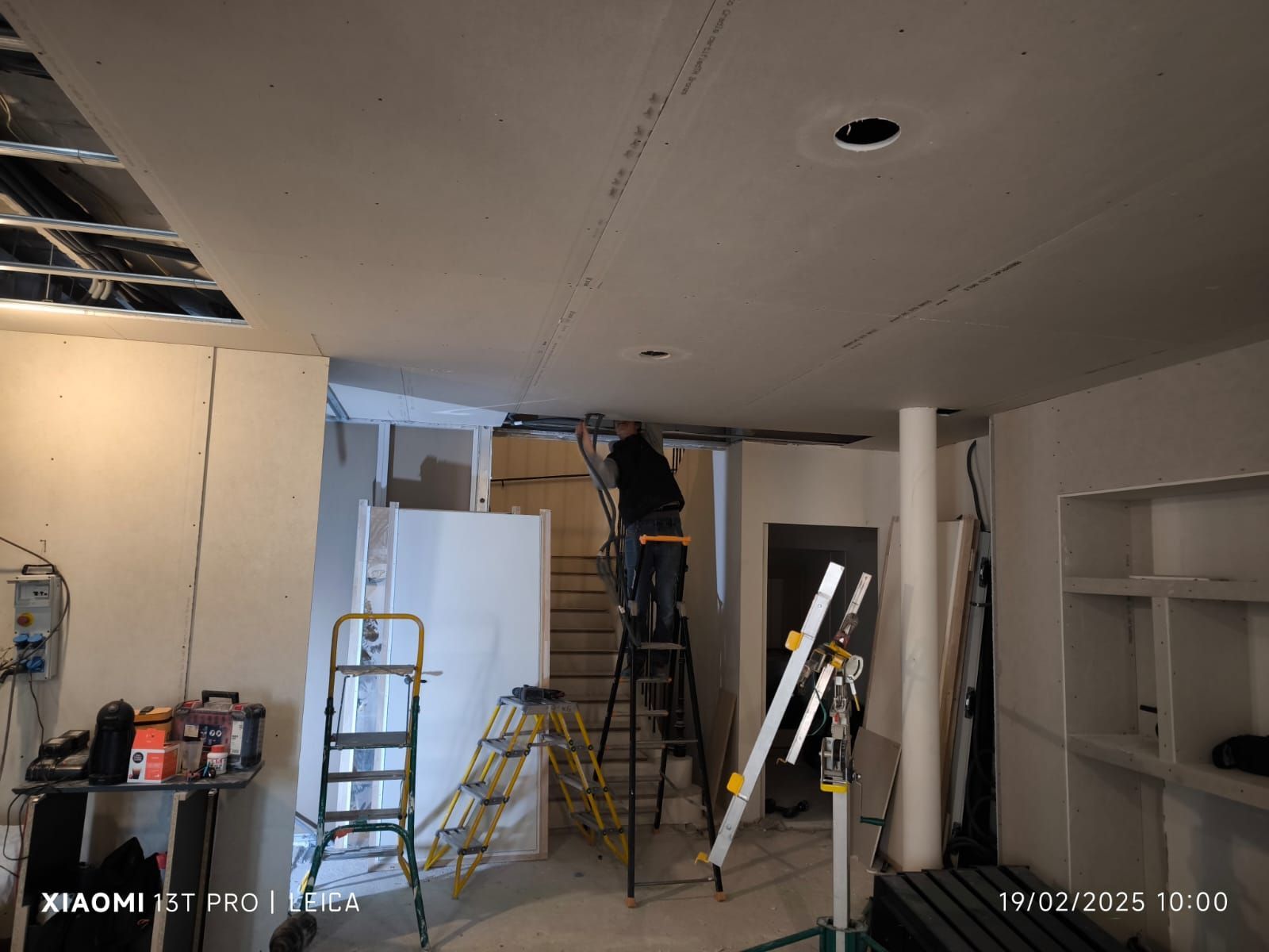 Ouvrier en train de tirer sur une gaine électrique sortant d'un faux plafond