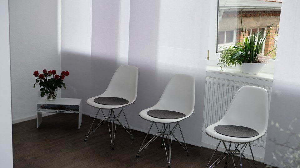 Wartezimmer mit weißen Stühlen und einem Tisch mit Rosen neben einem Fenster.